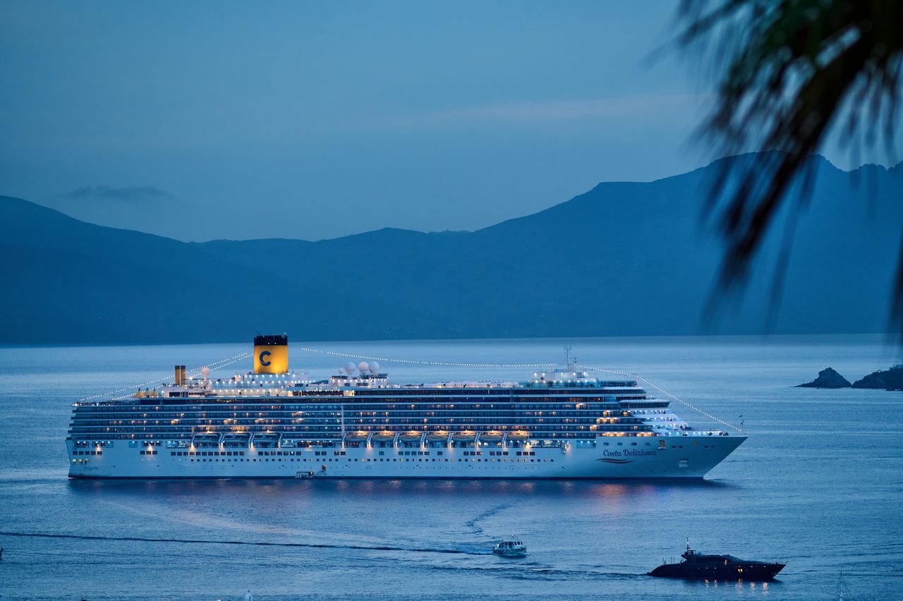 about-img-01 A beautifully illuminated cruise ship sails across the calm sea at dusk, framed by mountains.